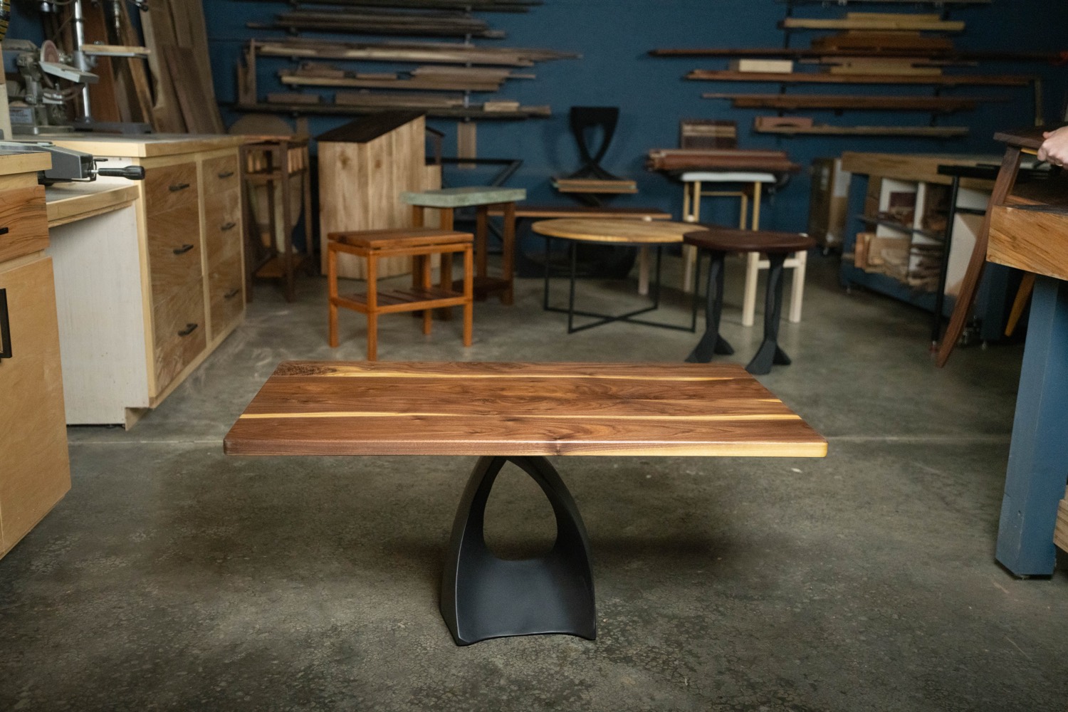 Live-edge walnut coffee table with a sculpted black base, among a group of finished tables