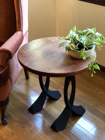 Round walnut end table with sculpted black steel legs beside an armchair