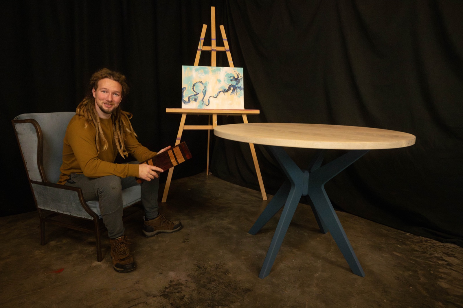 Raccoon Mountain Woodworks craftsman seated beside a round pedestal table in the workshop