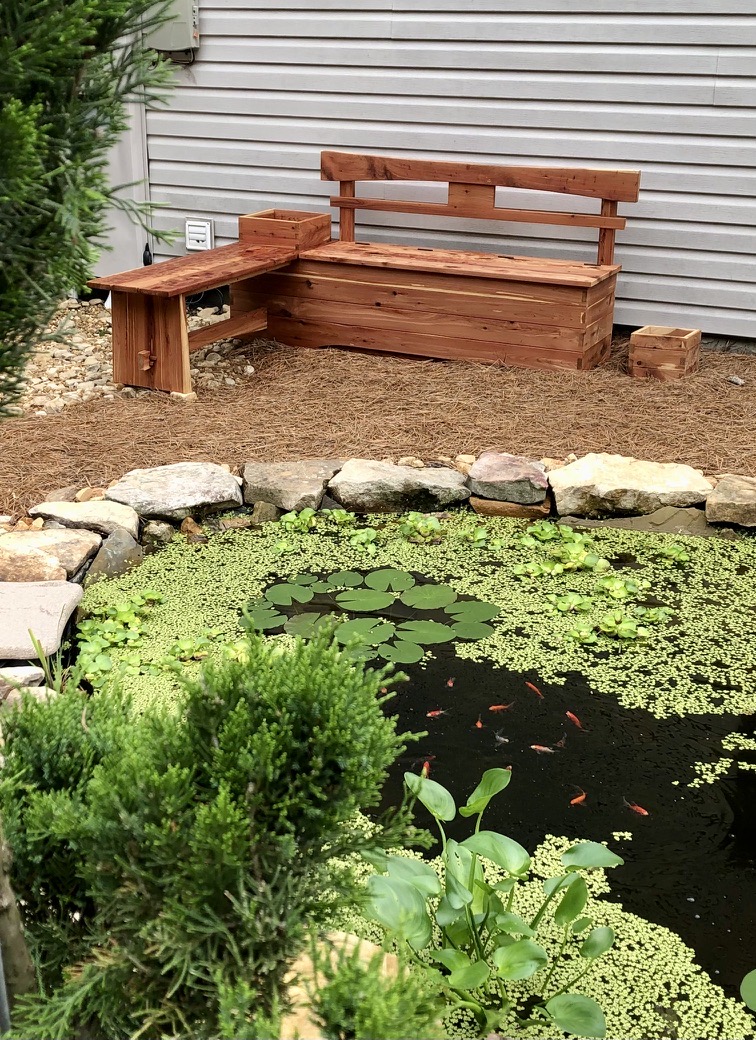 Cedar garden bench with an attached side table beside a koi pond